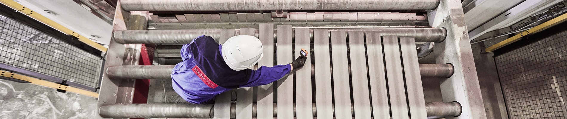 Worker in protective gear operates machinery, arranging metal bars in an industrial setting, viewed from above.